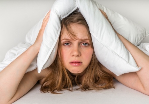 Tired woman covering her head with pillow
