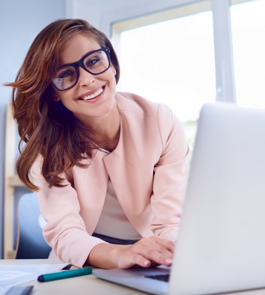 Smiling woman with glasses sitting at desk with laptop