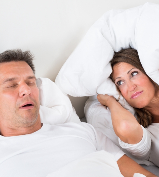 Woman covering her ears next to snoring man needing sleep apnea treatment
