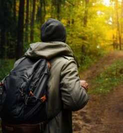 Person wearing beanie and backpack hiking through the woods