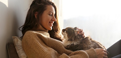 Young woman in turtleneck sweater petting cat on her lap