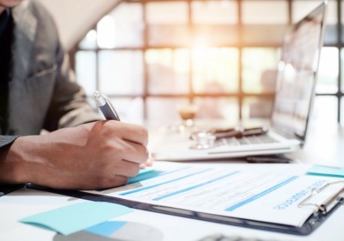 Person filling out paperwork at desk next to laptop