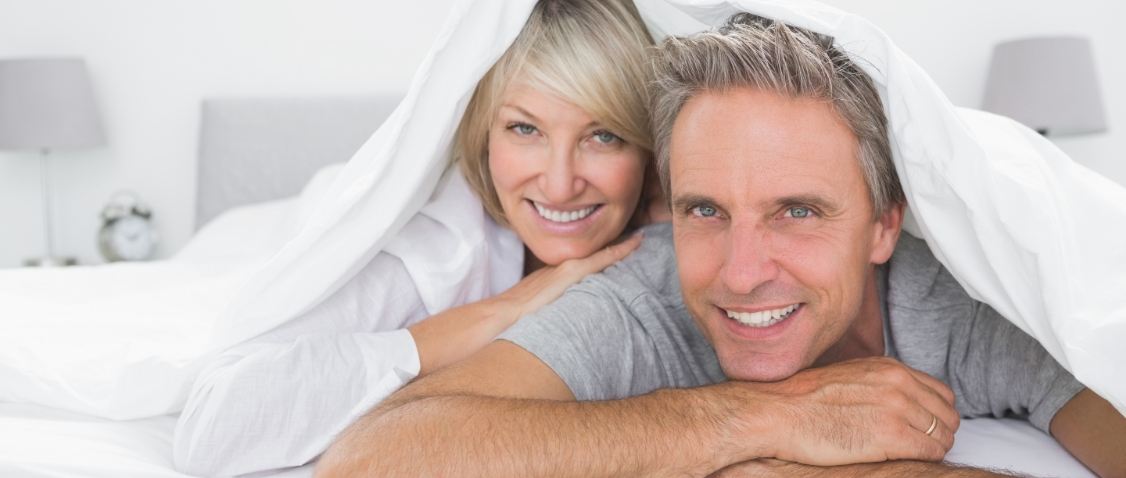 Older man and woman laying in bed on their stomachs and smiling after sleep apnea services in Glendale