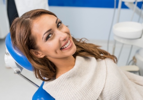 Woman in white sweater smiling in dental exam chair