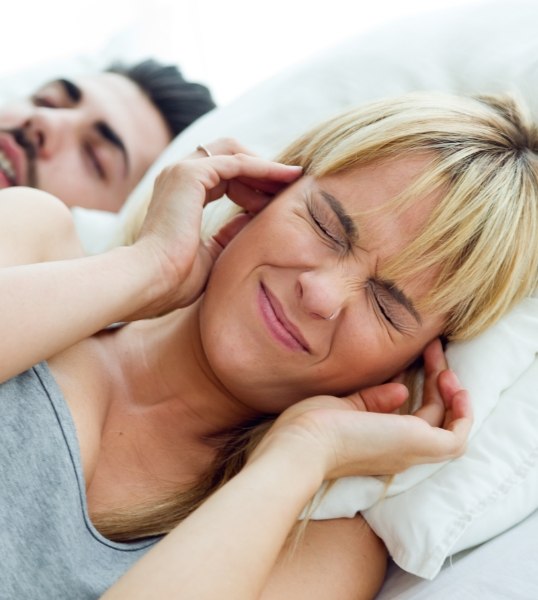 Woman covering her ears next to snoring man needing sleep apnea treatment