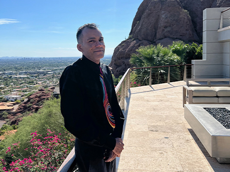 Ulysio in black dress shirt and colorful tie standing on balcony